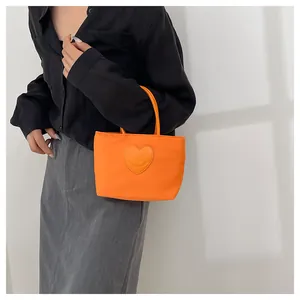 Detail of a minimalist orange nylon handbag featuring a heart-shaped smiley patch detail