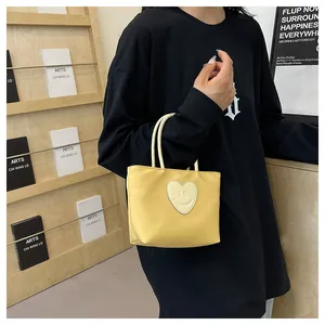 Detail view of a yellow tote bag with a smiley face heart patch and dual handles
