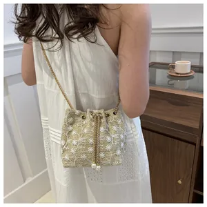 Chic beige straw bucket bag with floral embroidery and gold chain strap on model