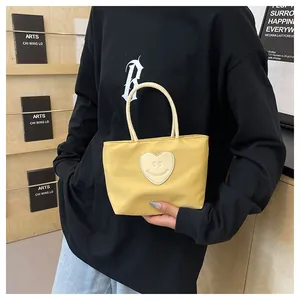Detail of a bright yellow nylon tote bag featuring a white heart smile patch and rope handle