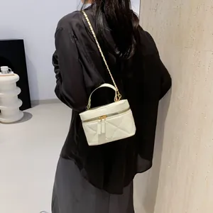 Cream quilted bucket bag with chain strap and top handle shown in minimalist interior