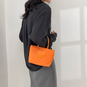 Orange nylon handbag with heart smiley patch shown in a minimalist outdoor setting