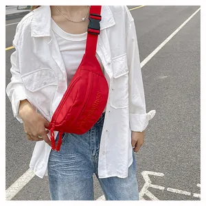 Detail of red nylon crossbody chest bag featuring embroidered text and adjustable strap