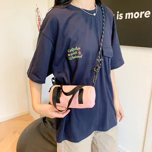 Pink cylindrical crossbody bag with black handles and striped shoulder strap in casual style