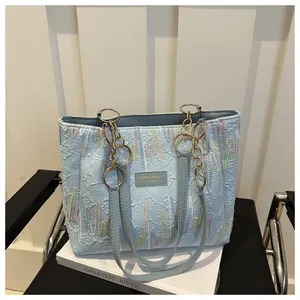 Détail d'un cabas bleu clair avec broderie multicolore et bandoulière à chaîne dorée