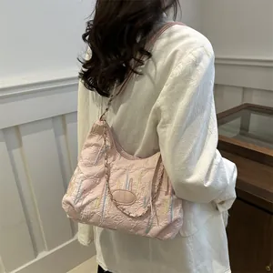 Sac hobo matelassé rose avec rayures colorées porté sur un manteau blanc chic
