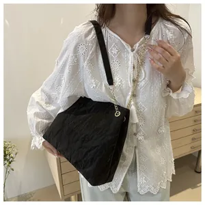 Détail du sac cabas plissé noir avec bandoulière dorée et accessoire pompon blanc
