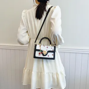 Sac bandoulière cerise avec boucle florale et poignée tressée sur fond blanc