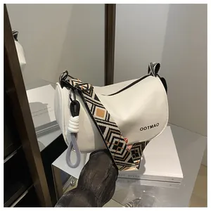 Détail du sac polochon en cuir crème avec bandoulière ethnique et pendentif à nœud