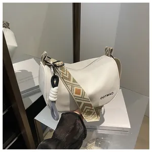 Vue détaillée du sac demi-lune blanc avec bandoulière brodée et pendentif tissé