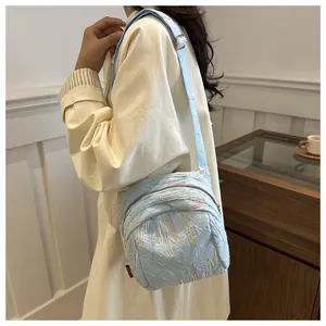 Détail d'un sac bandoulière bleu clair texturé avec broderies ondulées colorées