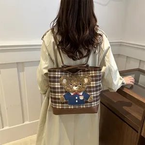 Plaid tote bag with 3D plush bear detail and brown leather straps worn by model