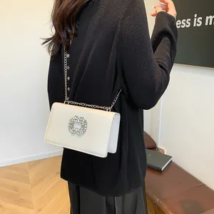 Sac à bandoulière blanc crème avec boucle en strass porté sur un haut noir