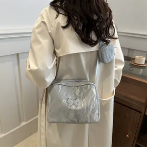 Silver metallic pleated crossbody bag with butterfly charm and small pouch on beige trench coat