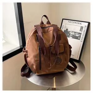 Detail view of water-resistant brown nylon backpack on table with front pocket and logo