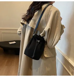 Dettaglio della borsa a secchiello nera con coulisse e tracolla in pelle su trench beige
