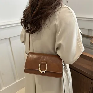 Retro caramel brown shoulder bag with a gold U-shaped buckle in a minimalist setting