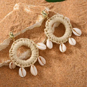 Bohemian woven raffia hoop earrings with shell pendants on a beach background