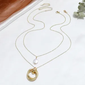 Detalle de collar de capas dorado con perla blanca y colgante de triple anillo en tela