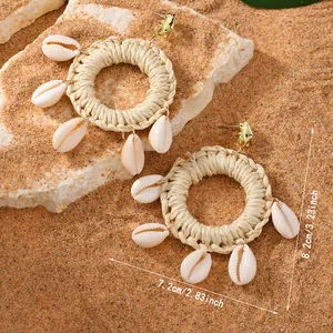 Detail view of woven raffia hoop earrings with cowrie shells and gold stud accents