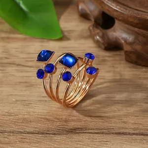 Goudkleurige gelaagde veerring met donkerblauwe edelstenen op een houten achtergrond