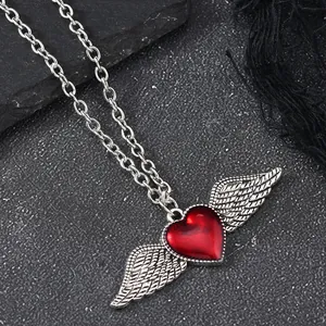 Macro detail of Gothic red heart pendant with silver wings on a dark stone texture