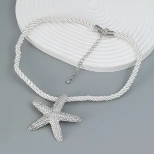 Macro detail of silver starfish pendant with textured finish on white woven cord necklace