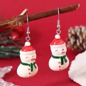 Detailed close-up of Christmas snowman earrings with red hats and green scarves on wood