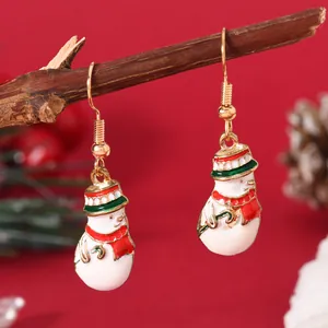 Detailed view of handmade enamel snowman Christmas earrings hanging on a rustic wooden branch