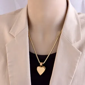 Golden heart pendant necklace with snake chain worn on a model in a beige suit