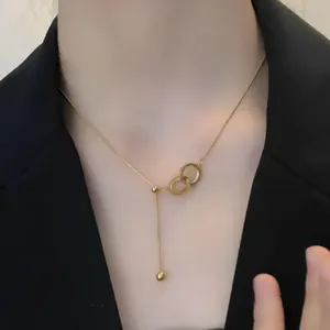 Close-up of interlocking metal logo pendant on a gold chain with a small gold bead