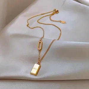 Détail du collier lingot d'or avec gravure 'GOLD' sur un fond en soie élégant