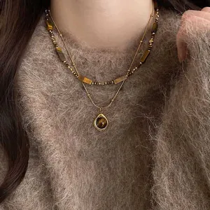 Gros plan du collier double rang doré avec pendentif oeil de tigre sur pull en mohair brun