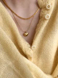 Dettaglio della collana a doppio strato con cuore dorato su maglione giallo