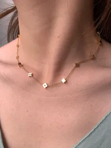 Detailed view of a gold four-leaf flower and square pendant necklace on a female model