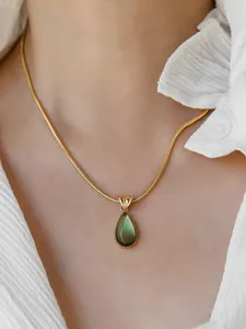 Close-up of elegant gold snake chain necklace with a green teardrop crystal pendant