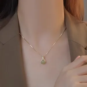 Dettaglio di un ciondolo con gemma verde e catena dorata indossato da una modella