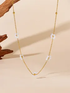 Detail of gold titanium floral necklace with small white pearl daisy pendants on beige background