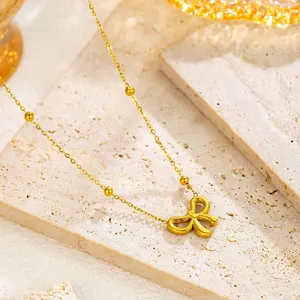 Elegant gold bow pendant necklace with bead accents on a minimalist stone background