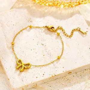 Elegant gold bow necklace in titanium steel with beads and lobster clasp on stone surface