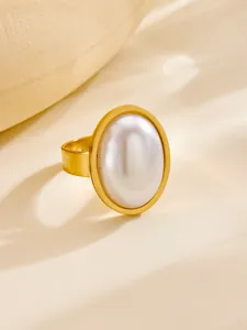 Macro view of gold-plated wide band ring featuring a large oval white faux pearl