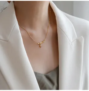 Close-up of golden bamboo necklace with leaf pendant on model wearing white blazer