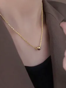 Detailed view of a gold ball pendant necklace worn with a stylish brown blazer jacket