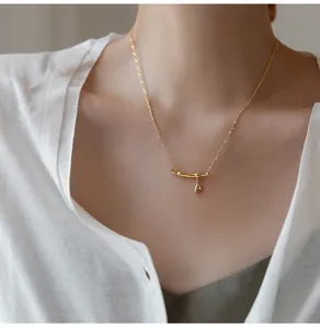 Close-up of a gold bamboo-shaped necklace with a small leaf pendant on a female model