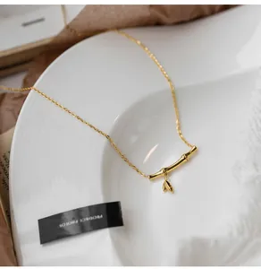 Detail of golden bamboo pendant with leaves and polished cross chain on textured white plate