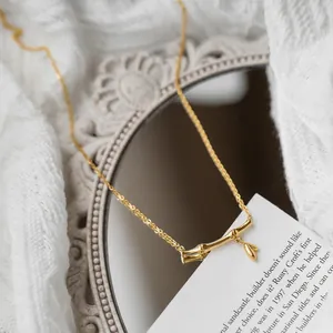 Elegant gold bamboo joint pendant necklace with leaf charm on a vintage mirror