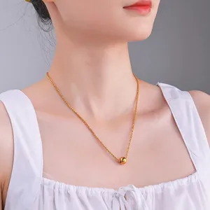 Close-up of a polished gold bead pendant on a braided chain necklace worn by a model