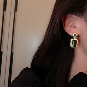 Close-up of model wearing gold earrings with emerald green crystals and zircon accents