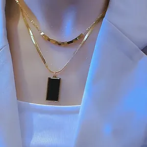 Detalle de collar dorado de doble capa con cuentas cuadradas y colgante rectangular negro