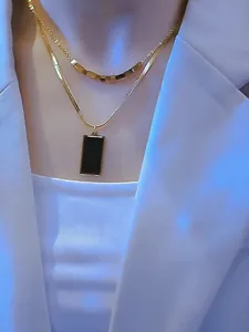 Detalle de collar doble capa dorado con colgante cuadrado negro y cadena de serpiente fina